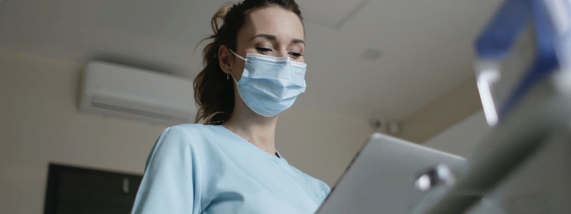 Healthcare worker in scrubs and face mask using a tablet in a clinical setting